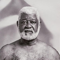 black and white portrait of man with beard, blurred hand pattern in background.