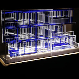 3D geometric acrylic model, rectangular windows and blue features, in a glass case with wooden back under LED lights.