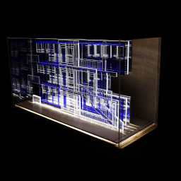 3D geometric acrylic model, rectangular windows and blue features, in a glass case with wooden back under LED lights.