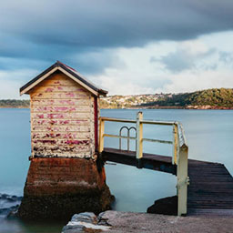 small weathered house, board walk with railing, sitting on sea landscape.