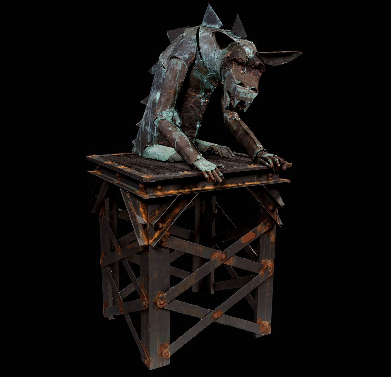 Rusty metal gargoyle statue sitting on raised metal structure.