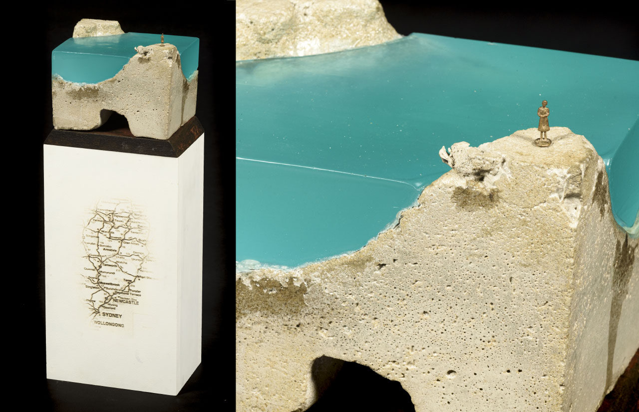 white plinth with map print, cement block sitting on top with blue accent and miniature bronze figure of a woman.