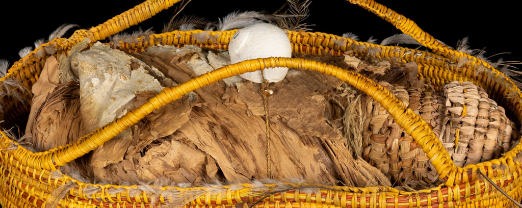 Woven sculpture of headless womans torso with feathers on neck and hips and woven sculpture of baby basket