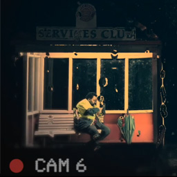 Still shot of a man sitting on a bench shown from the perspective of the surviellance camera.