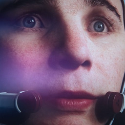 Still shot of extreme close up of male face with blue eyes and microphone at lips.